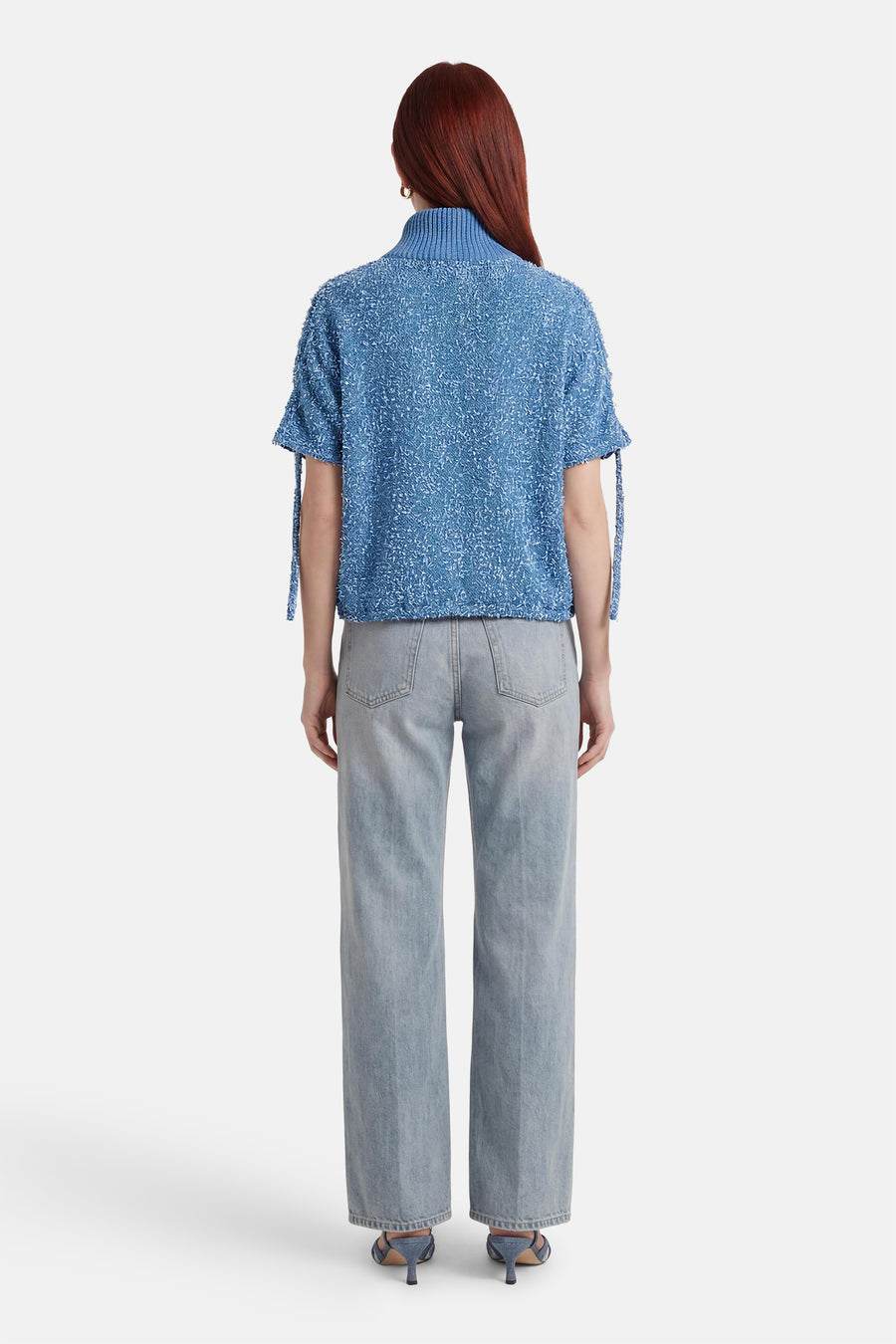Veste courte bleue texturée de ADORE, avec des liens décoratifs aux manches, portée avec un jean et des chaussures assorties.