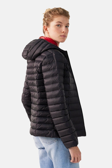 Veste de pluie noire de JOTT, avec capuche, portée avec un pull rouge et un jean bleu clair.