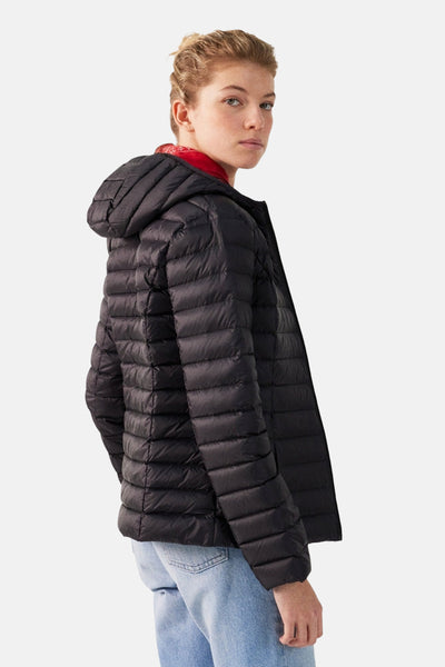 Veste de pluie noire de JOTT, avec capuche, portée avec un pull rouge et un jean bleu clair.