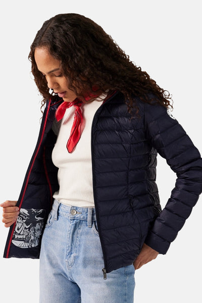 Veste de pluie bleue de JOTT, portée avec un foulard rouge, un pull blanc et un jean clair.