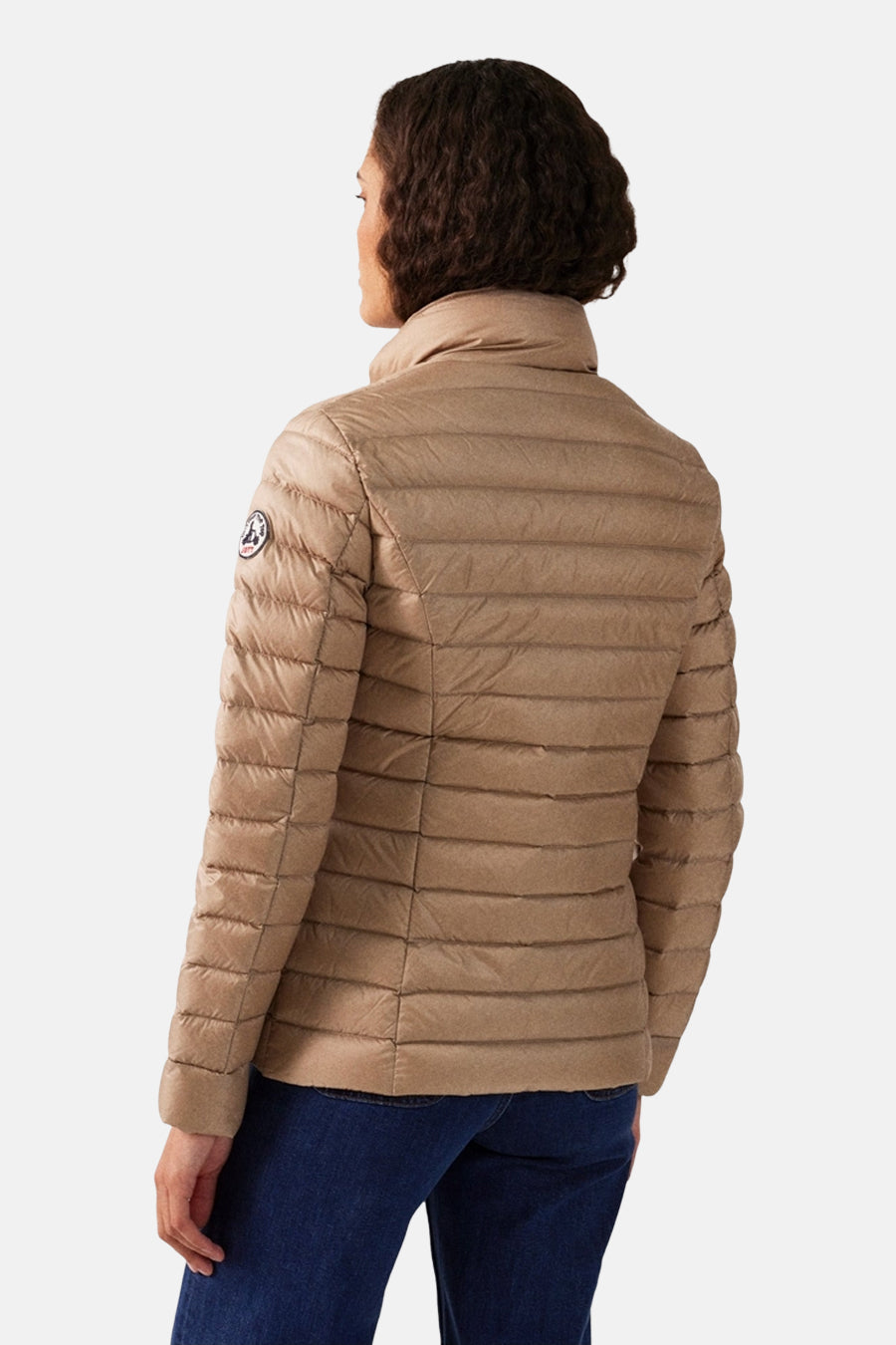 Beige regenjas van JOTT, gewatteerd met een opstaande kraag, gedragen met een donkerblauwe jeans.