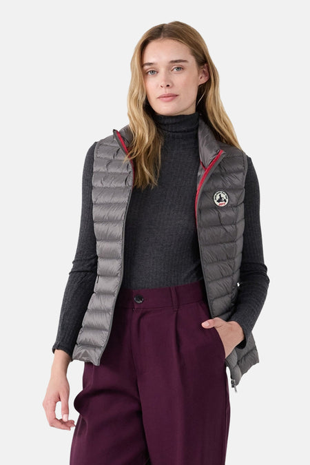 Grijze mouwloze jas van JOTT, met rode voering, gedragen over een donkergrijze trui en een bordeauxrode broek.