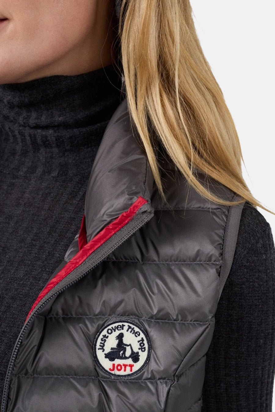 Veste sans manches grise de JOTT, bordure rouge visible et logo rond cousu sur le devant.