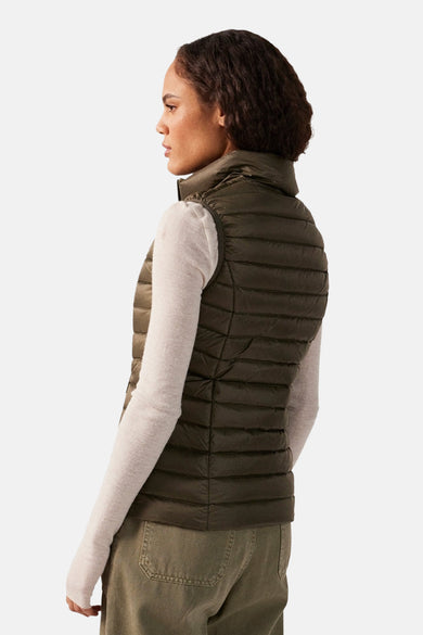 Veste sans manches kaki de JOTT, matelassée avec col montant, portée sur un t-shirt à manches longues et un pantalon.