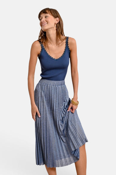 Molly Bracken 3/4 blauwe rok, geplooid met een metallic effect, gedragen met een bijpassend hemdje en gouden sieraden.