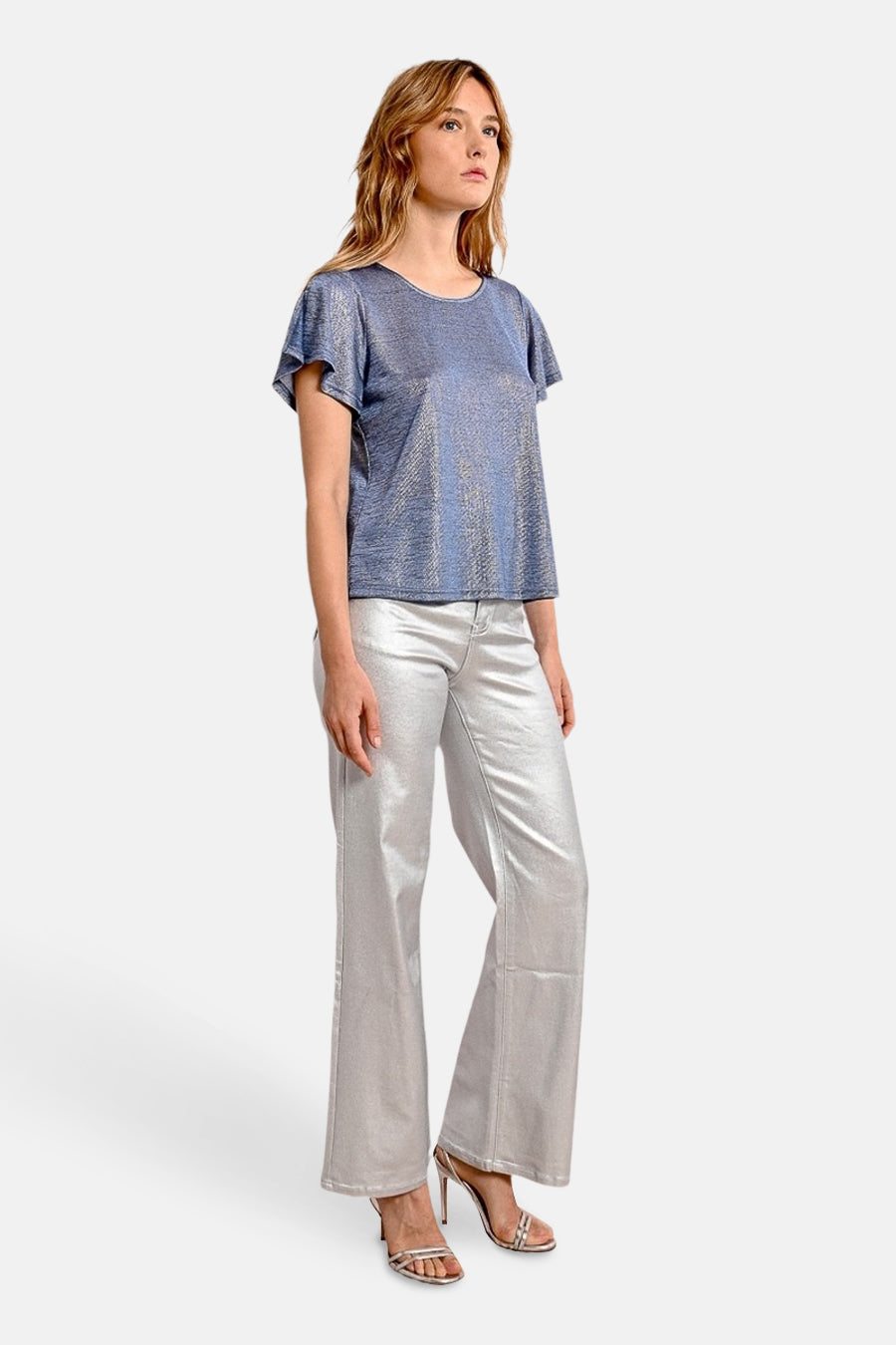 T-shirt bleu à manches courtes de Molly Bracken, avec un tissu texturé brillant, porté avec un pantalon argenté et des sandales à talons.