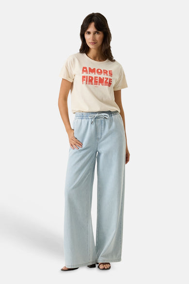 Ecru short-sleeve t-shirt with bold red "AMORE FIRENZE" graphic, worn with light blue wide-leg jeans and black sandals, full-body front view.