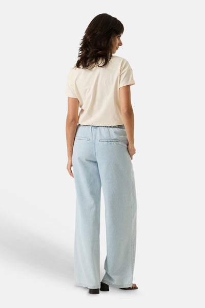 Ecru short-sleeve t-shirt from back view, plain cotton fabric, paired with light blue wide-leg jeans and black sandals