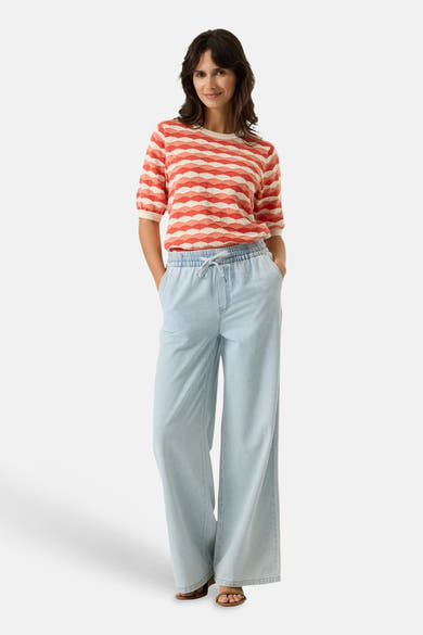 Pull multicolore col rond, de GARCIA, à rayures horizontales ondulées, porté avec un pantalon ample en denim bleu clair.
