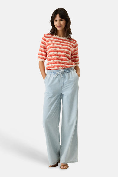 Pull multicolore col rond, de GARCIA, à rayures horizontales ondulées, porté avec un pantalon ample en denim bleu clair.
