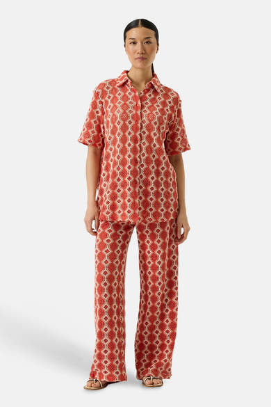 Pantalon orange van GARCIA, avec un motif géométrique ajouré, porté avec une chemise assortie et des sandales dorées.