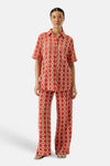 Pantalon orange van GARCIA, avec un motif géométrique ajouré, porté avec une chemise assortie et des sandales dorées.