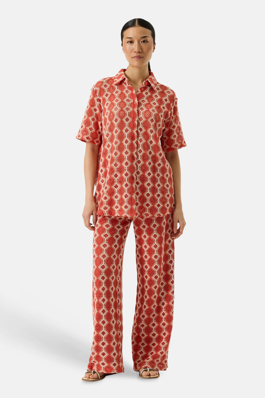 Pantalon orange van GARCIA, avec un motif géométrique ajouré, porté avec une chemise assortie et des sandales dorées.