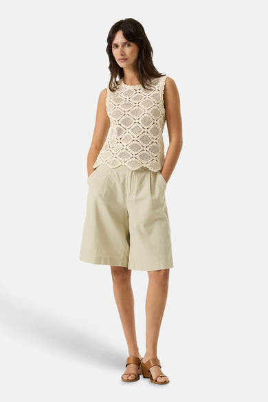 Bermuda beige de GARCIA, avec des poches et des plis sur le devant, porté avec un top ajouré sans manches et des sandales marron à talons.
