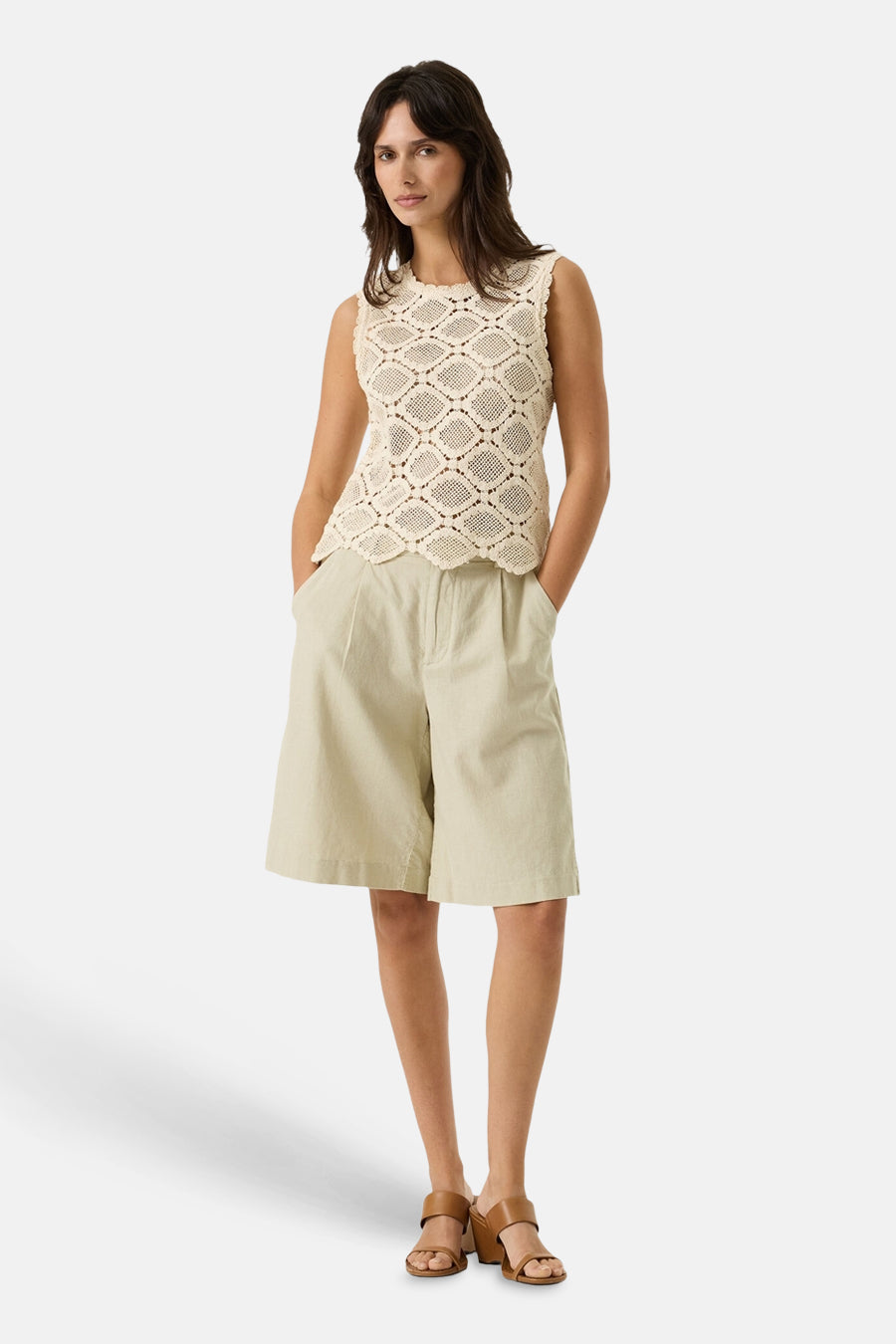 Bermuda beige de GARCIA, avec des poches et des plis sur le devant, porté avec un top ajouré sans manches et des sandales marron à talons.
