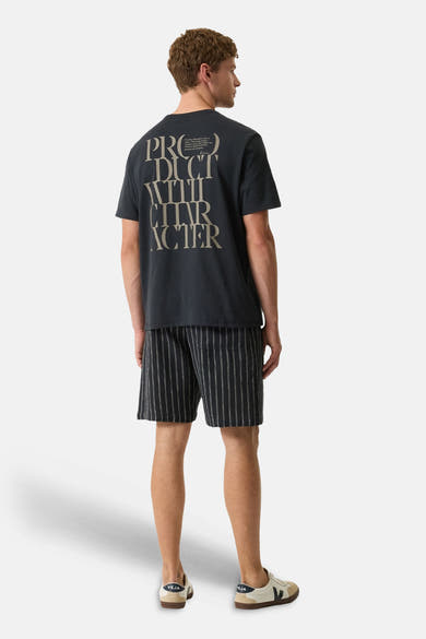 T-shirt noir à manches courtes de GARCIA avec inscription "PRODUCT WITH CHARACTER" au dos, porté avec un short rayé et des baskets claires.