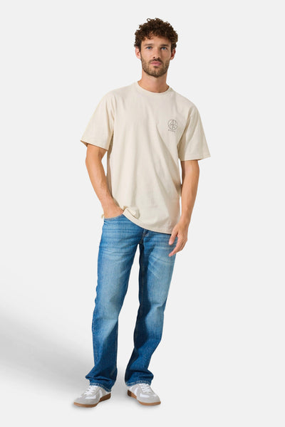 Beige T-shirt met korte mouwen van GARCIA, met een cirkelvormig logo, gedragen met een blauwe jeans en grijze sneakers.