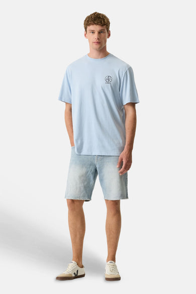 Lichtblauw T-shirt van GARCIA met een cirkelvormig logo, gedragen met een verbleekte spijkerbroekshort en lichte sneakers.