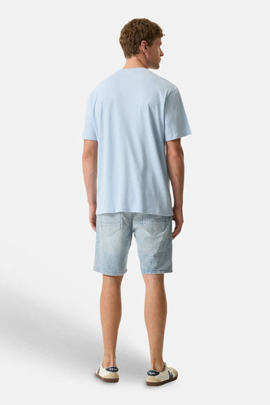 Blauw T-shirt van GARCIA, achterkant, gedragen met een lichtblauwe spijkerbroek met korte pijpen en lichte sneakers.