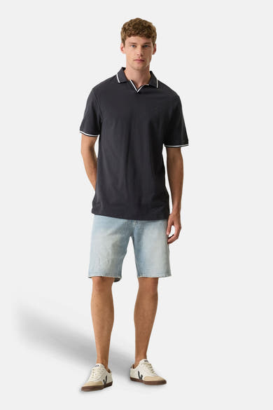 Polo bleu foncé de GARCIA à liserés blancs sur col et manches, porté avec short en jean et baskets.