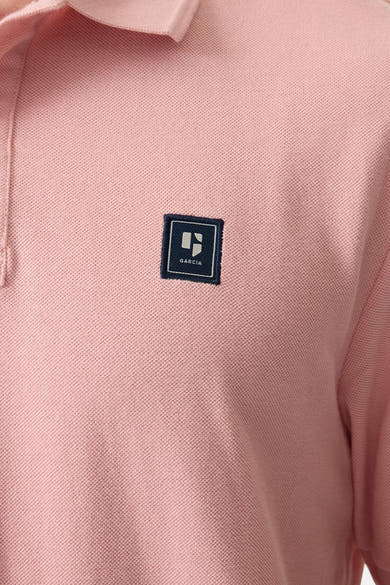 Polo rose en maille piquée de GARCIA, avec un écusson carré bleu marine cousu sur la poitrine.