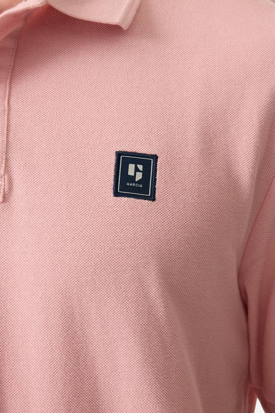 Polo rose en maille piquée de GARCIA, avec un écusson carré bleu marine cousu sur la poitrine.