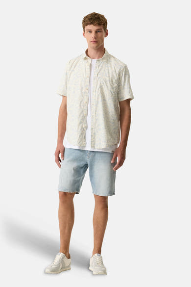 Chemise à manches courtes multicolore de GARCIA à motif floral beige et bleu clair, portée avec un t-shirt blanc, un short en jean et des baskets claires.
