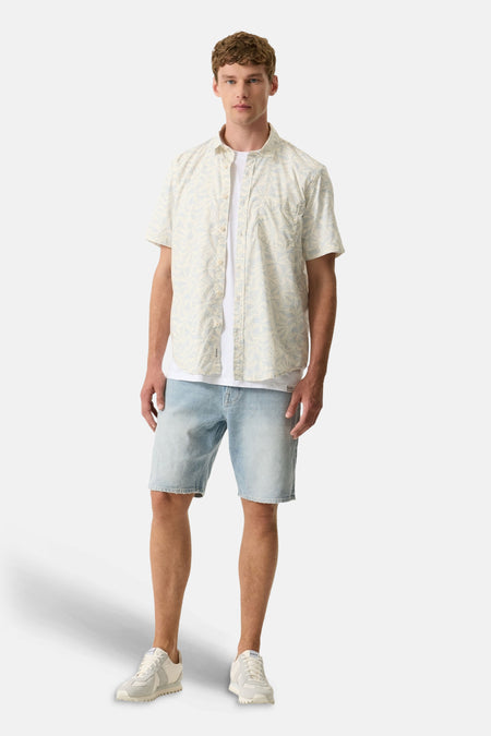 Chemise à manches courtes multicolore de GARCIA à motif floral beige et bleu clair, portée avec un t-shirt blanc, un short en jean et des baskets claires.