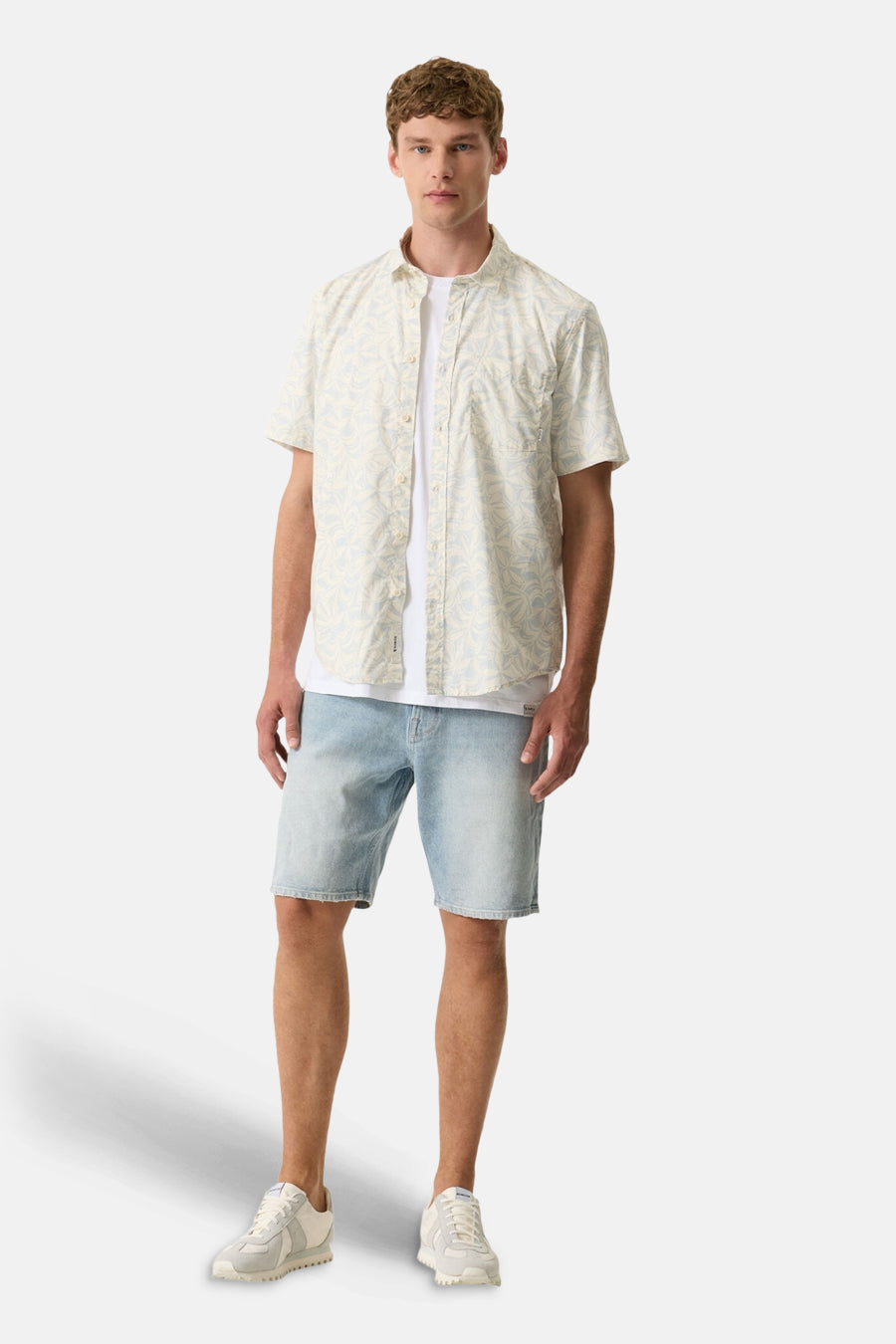 Chemise à manches courtes multicolore de GARCIA à motif floral beige et bleu clair, portée avec un t-shirt blanc, un short en jean et des baskets claires.