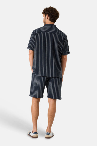 Marineblauw overhemd met korte mouwen en fijne witte strepen van GARCIA, van achteren gedragen met bijpassende korte broek en lichte sneakers.