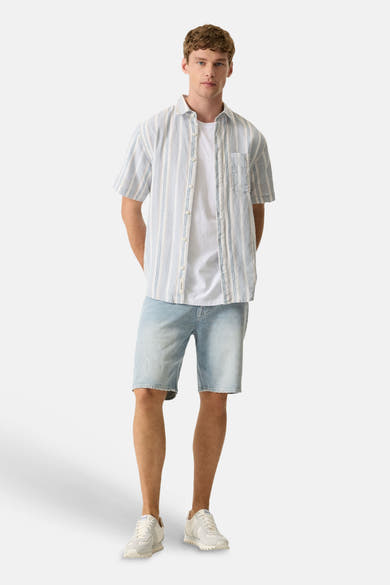 Chemise bleue de GARCIA à manches courtes, rayée de blanc et de bleu clair, portée sur un t-shirt blanc avec un short en jean.