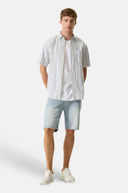 Chemise bleue de GARCIA à manches courtes, rayée de blanc et de bleu clair, portée sur un t-shirt blanc avec un short en jean.