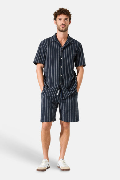 Short rayé bleu marine de GARCIA avec cordon de serrage, porté avec une chemise assortie et des baskets blanches.