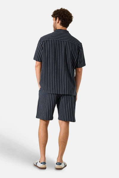 Short bleu marine rayé de GARCIA, avec rayures blanches, porté de dos avec un t-shirt assorti.