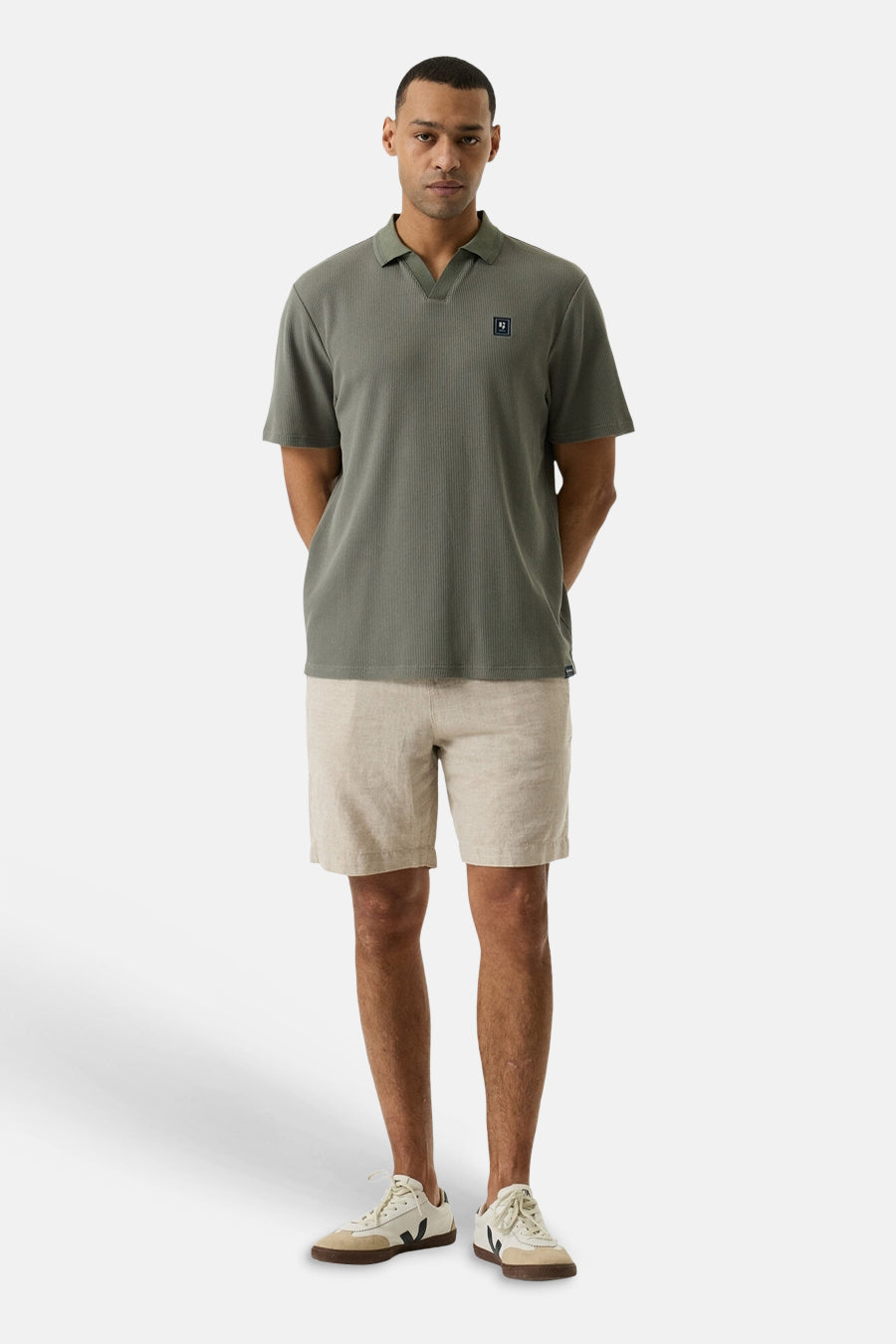 Short beige de GARCIA en tissu texturé, porté par un homme avec un polo vert olive et des baskets.