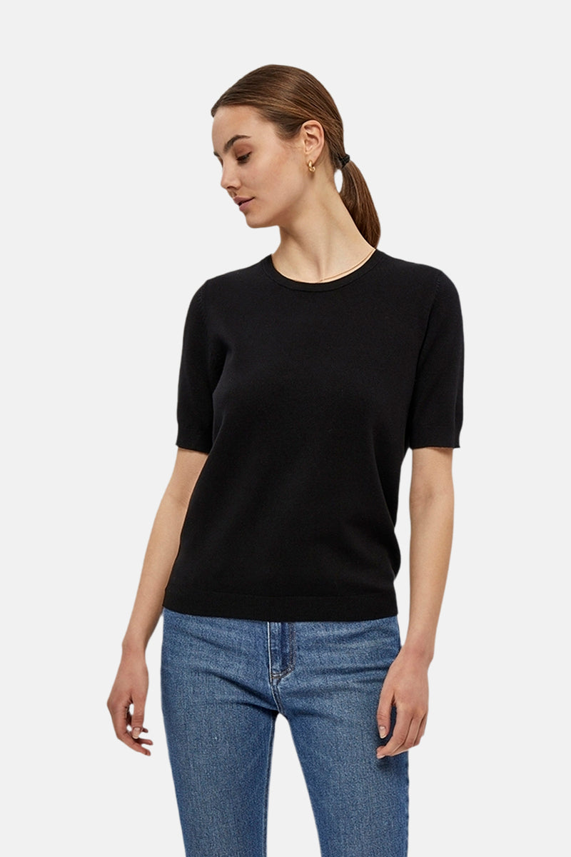 Pull à col rond noir de PEPPERCORN, porté avec un jean bleu et des boucles d'oreilles dorées.