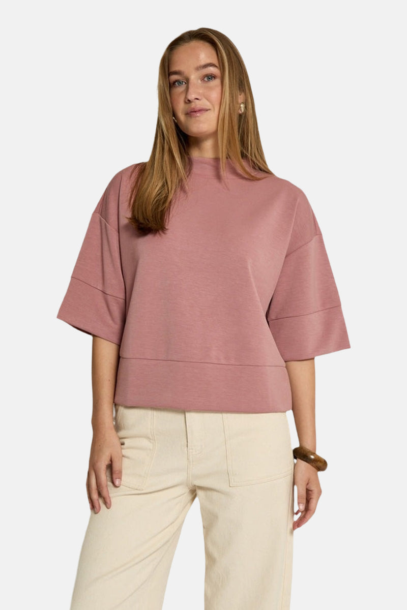 Sweat rose de PEPPERCORN, avec des manches courtes amples et un ourlet droit, porté avec un pantalon couleur crème.
