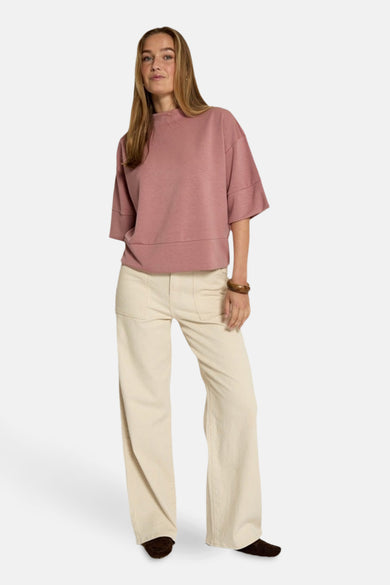 Sweat rose de PEPPERCORN, avec des manches courtes et une encolure montante, porté avec un pantalon beige ample.