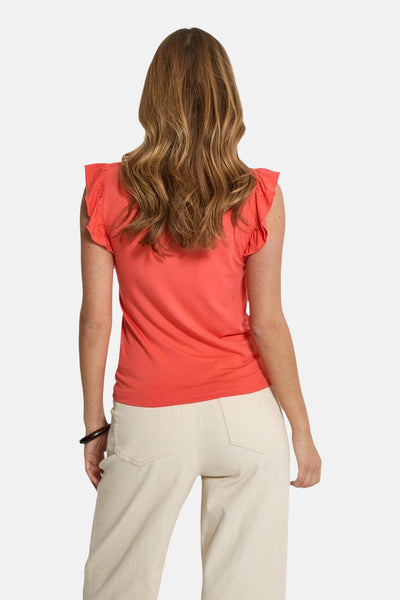 Top sans manches corail de PEPPERCORN avec manches à volants, porté avec un pantalon clair.