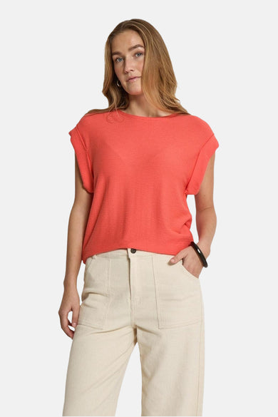 T-shirt corail à manches courtes de PEPPERCORN, porté avec un pantalon taille haute couleur crème et un bracelet noir.