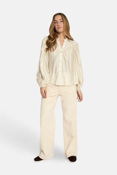 Ecru blouse met lange mouwen van PEPPERCORN, met opstaande kraag en knopen, gedragen met een beige broek met wijde pijpen.