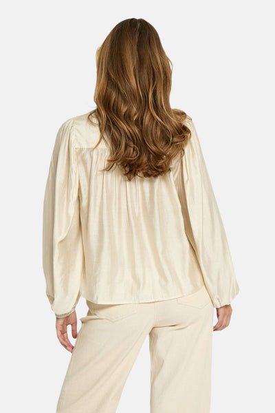 Blouse à manches longues écru de PEPPERCORN, avec un tissu texturé et des manches bouffantes, vue de dos, portée avec un pantalon beige.