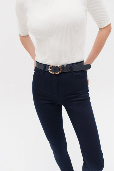 Gekleurde blauwe broek van CAROLL, gedragen met een riem met gouden gesp en een witte geribbelde trui.
