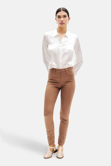 Pantalon coloré cognac de CAROLL, porté avec une chemise blanche à poches et des sandales.