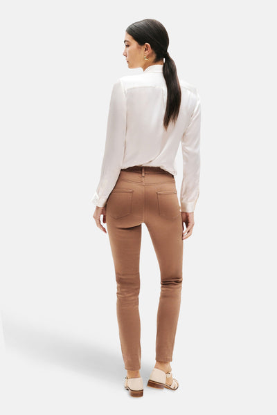 Pantalon coloré cognac de CAROLL, porté avec un chemisier blanc et des chaussures beiges, vue de dos.
