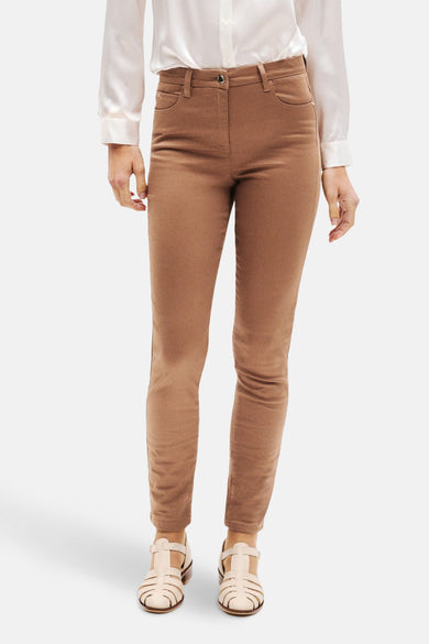 Pantalon coloré cognac de CAROLL, avec poches avant, porté avec une chemise blanche et des sandales.