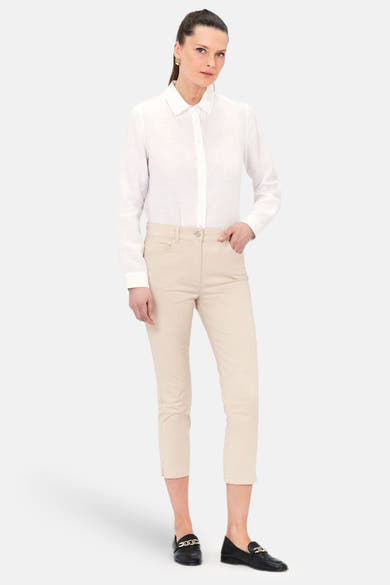 Chino 7/8 beige de CAROLL, porté avec une chemise blanche et des mocassins noirs à chaîne dorée.
