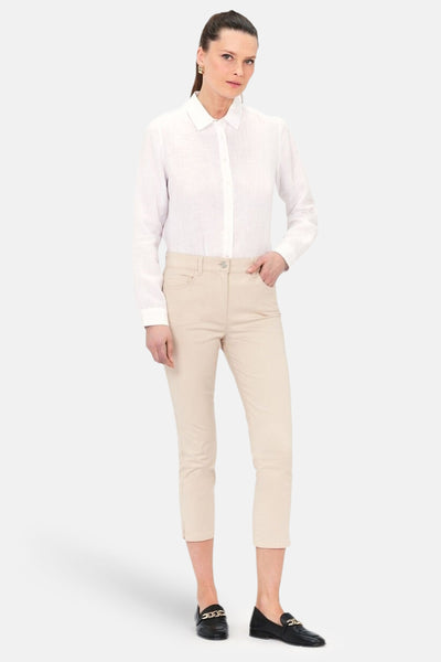 Chino 7/8 beige de CAROLL, porté avec une chemise blanche et des mocassins noirs à chaîne dorée.
