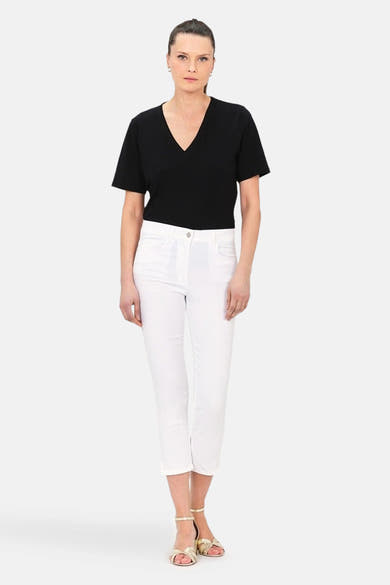 Pantalon chino 7/8 blanc de CAROLL, porté avec un t-shirt noir et des sandales dorées.