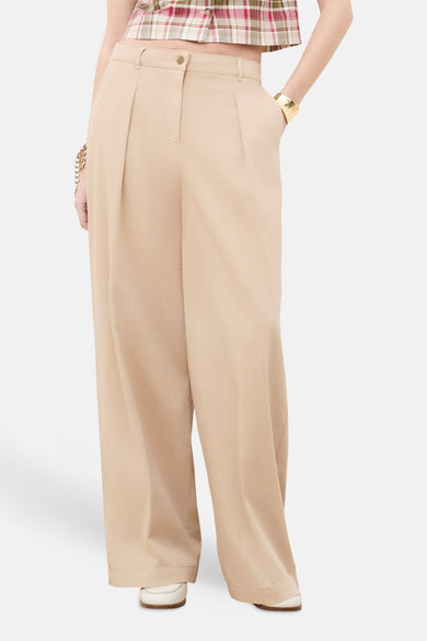 Chino beige de CAROLL, large et plissé, porté avec un crop top à carreaux, un bracelet doré et des mocassins blancs.